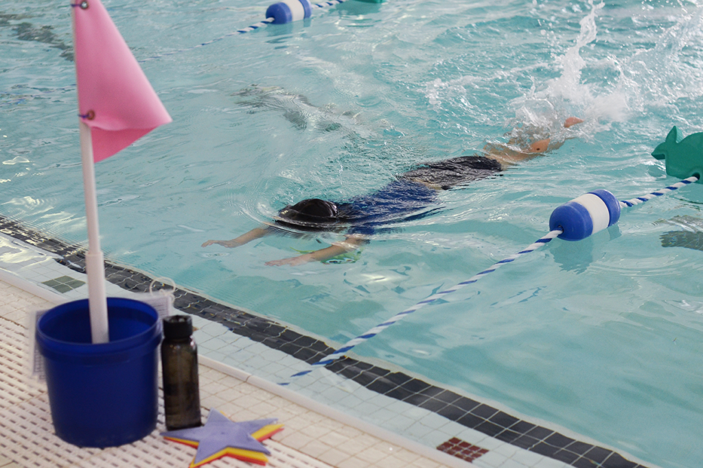 stroke evolution photo, instructor in pool with child learning float and kick skills at little otter