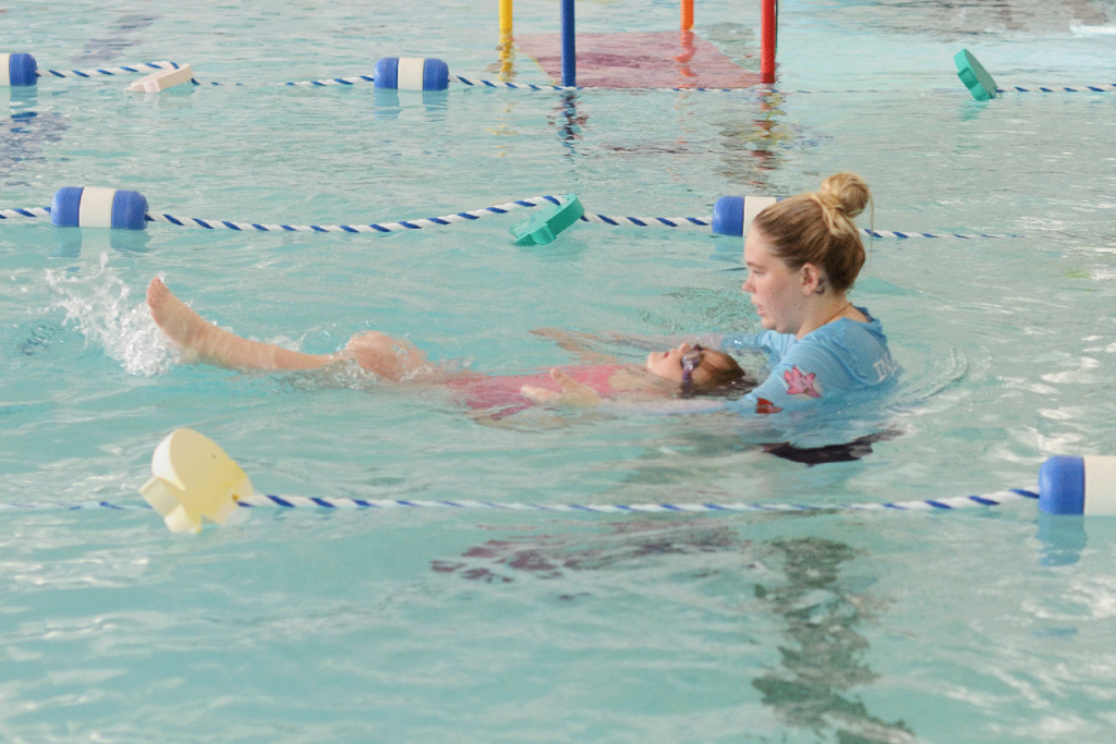 Skills development photo, instructor in pool with child learning float and kick skills at little otter